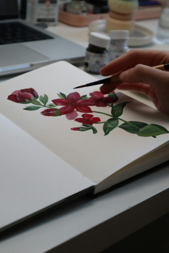 pexels photo 14748147 14748147 Close-up of artistic hand painting vibrant red flowers in a notebook.