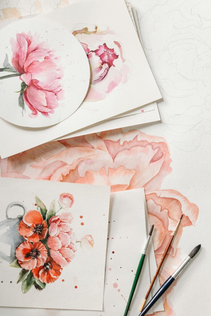 Home Colorful watercolor paintings of flowers with paintbrushes on white paper.